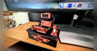 Fotografía oficial del montaje completo de Tiny Engineer, con cuerpo naranja, mesa propia y campana, sobre un escritorio.