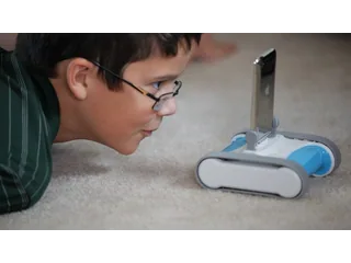 Un niño observa un Romo azul y blanco con un teléfono colocado en su base de orugas.