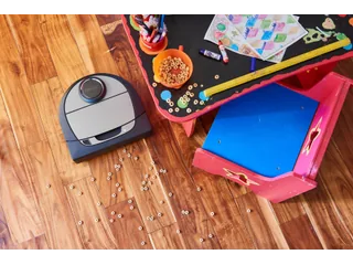 Imagen oficial del Neato Botvac D7 Connected en un suelo de madera junto a una mesa infantil.