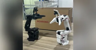 Dos brazos SO-ARM100 completos, uno negro y otro blanco, fotografiados junto a una caja WowRobo.