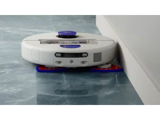 Fotografía oficial del Dyson R2 Nurovi Wash+Dry blanco fregando junto a una pared, con las dos mopas triangulares visibles.