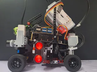 Fotografía del Team Terminator de su coche robot completo visto de lado, con chasis LEGO, ruedas negras, sensores y luces rojas.