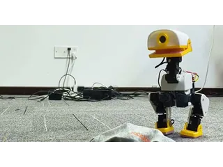 Fotograma oficial de XGO-Duck blanco y amarillo, de pie sobre una alfombra junto a una gorra y con la electrónica visible
