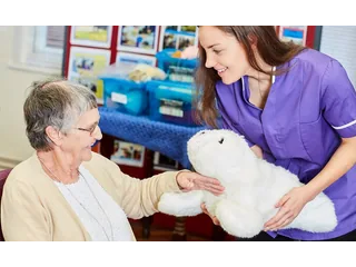 Una mujer sostiene PARO, la foca robótica blanca, junto a una profesional en un centro de cuidados.