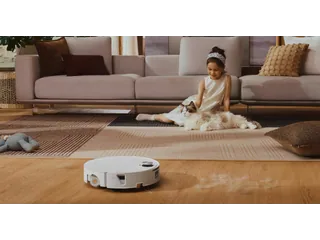 Fotografía promocional oficial del Roborock Saros 20 Flow blanco sobre suelo de madera, junto a una alfombra con una niña y un gato.