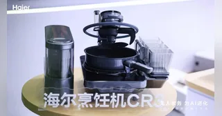 Imagen oficial de Haier del robot de cocina CR3 completo sobre una mesa amarilla, con los módulos de ingredientes y cocción.