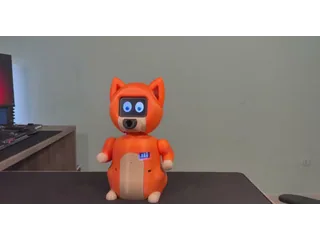 Nuvi, robot naranja con orejas de perro, ojos animados en una pantalla y brazos cortos, sobre una mesa.