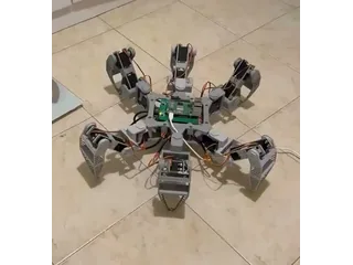 Fotograma recortado del inicio del vídeo de mike-tr, con el hexápodo completo de seis patas grises sobre suelo claro.