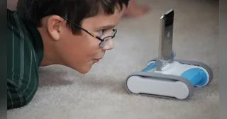 Un niño observa un Romo azul y blanco con un teléfono colocado en su base de orugas.