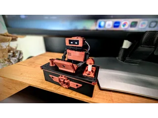 Fotografía oficial del montaje completo de Tiny Engineer, con cuerpo naranja, mesa propia y campana, sobre un escritorio.
