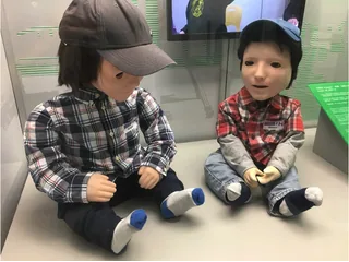 Dos robots Kaspar sentados, fotografiados como parte de una exposición.