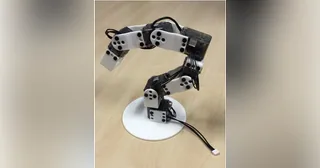 Brazo Poppy Ergo Jr con piezas blancas impresas en 3D y motores transparentes sobre una mesa de madera
