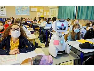 Buddy blanco con pantalla de videollamada junto a alumnos en un aula.