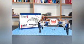 Fotografía oficial de H.I.R.O. TR-01-A completo, con cuatro patas y cuerpo blanco, sobre una mesa de montaje con la caja del kit.