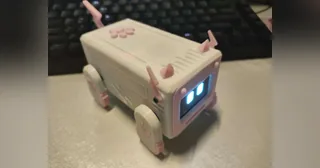 Fotografía del constructor de Xiaozhi ESP32 Pet completo, con carcasa rosa, pantalla facial y cuatro patas, sobre un escritorio.