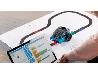 Robot Makeblock mBot2 sobre una pista de líneas junto a un portátil con programación por bloques, en una fotografía oficial de una actividad.