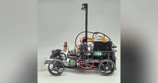 Fotografía de Double-X de su coche robot completo visto de lado, con estructura de tres niveles y cámara en un soporte alto.