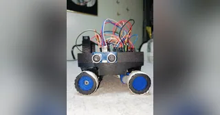 Fotografía de Vitality de su coche robot completo, con cuatro ruedas azules, electrónica visible y sensor ultrasónico lateral.