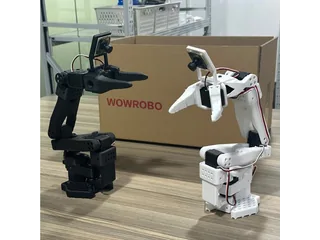 Dos brazos SO-ARM100 completos, uno negro y otro blanco, fotografiados junto a una caja WowRobo.