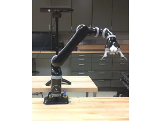 Fotografía completa del brazo Kinova MICO de seis ejes y pinza de dos dedos, fijado con su base a una mesa de laboratorio.