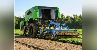 TREKTOR verde completo trabajando en una parcela, con un implemento agrícola azul conectado.