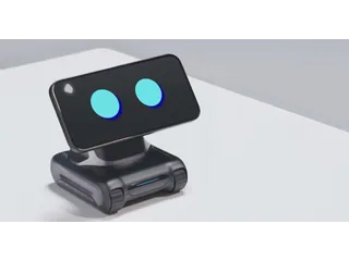 Fotograma oficial de un LOOI negro sobre una mesa blanca, con un teléfono en horizontal que muestra dos ojos azules.