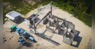 Vista aérea de una impresora COBOD BOD3 trabajando sobre los muros de un edificio en Indonesia, junto a su sistema de suministro de material.