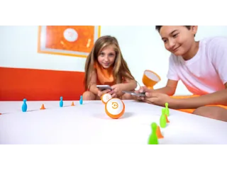 Dos niños controlan robots Sphero Mini naranjas con dispositivos móviles entre bolos y conos sobre una mesa, en una fotografía oficial de Sphero.