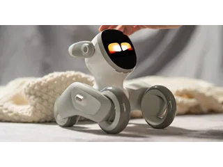 Una mano acaricia la cabeza de Loona Petbot, con los ojos iluminados y las cuatro ruedas apoyadas sobre una superficie junto a una manta, en una fotografía oficial.