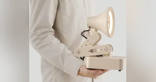Fotografía oficial de Autonomous Lamp de color arena, con el aro luminoso encendido, sostenido por una persona con jersey claro.