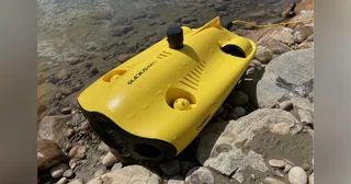 GLADIUS MINI S amarillo completo sobre rocas junto al agua, con su cable conectado.