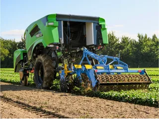 TREKTOR verde completo trabajando en una parcela, con un implemento agrícola azul conectado.