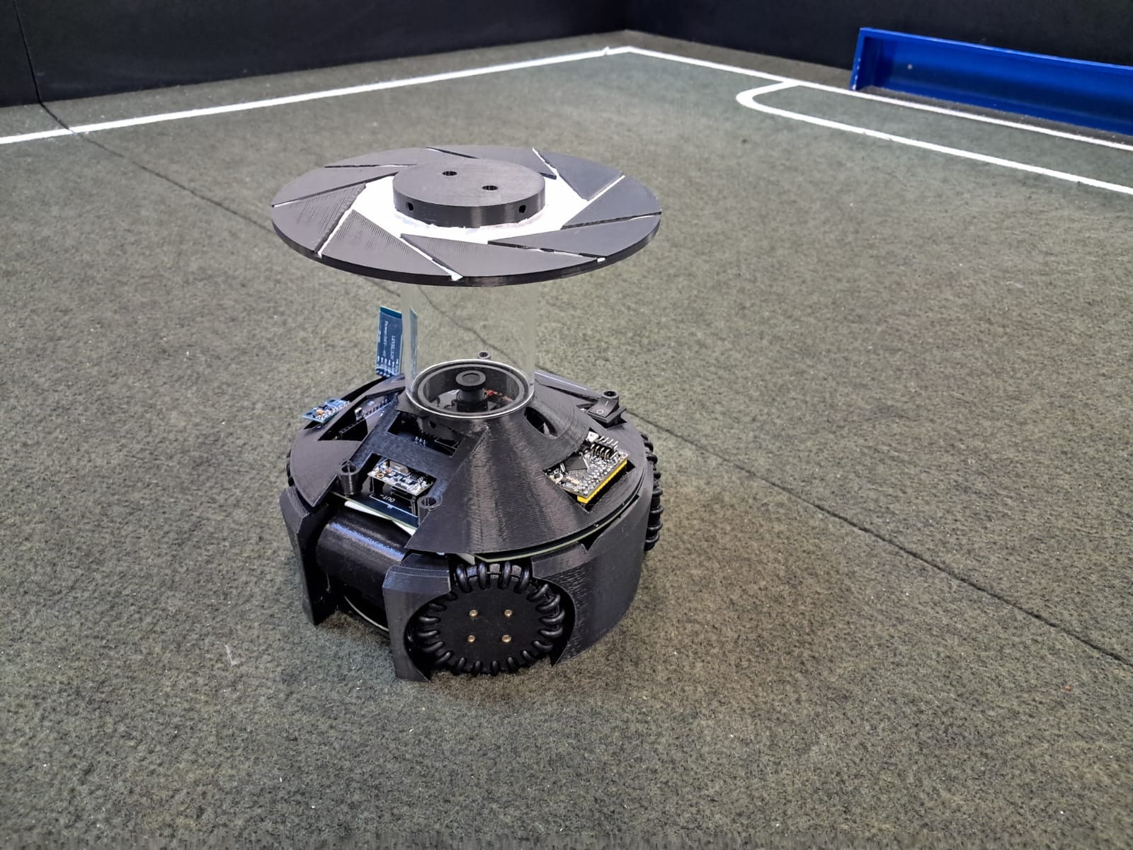 Fotografía de Aperture Open publicada en su cartel de 2025 del robot completo sobre el campo, con espejo superior y ruedas propias.