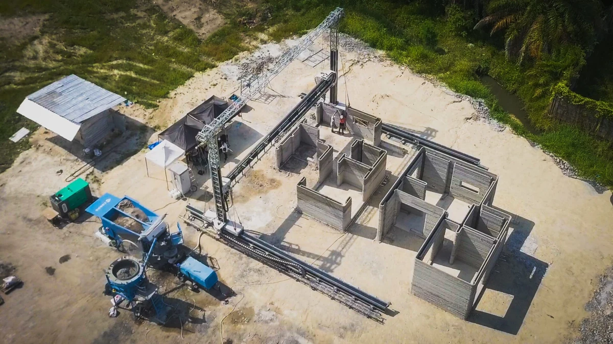 Vista aérea de una impresora COBOD BOD3 trabajando sobre los muros de un edificio en Indonesia, junto a su sistema de suministro de material.