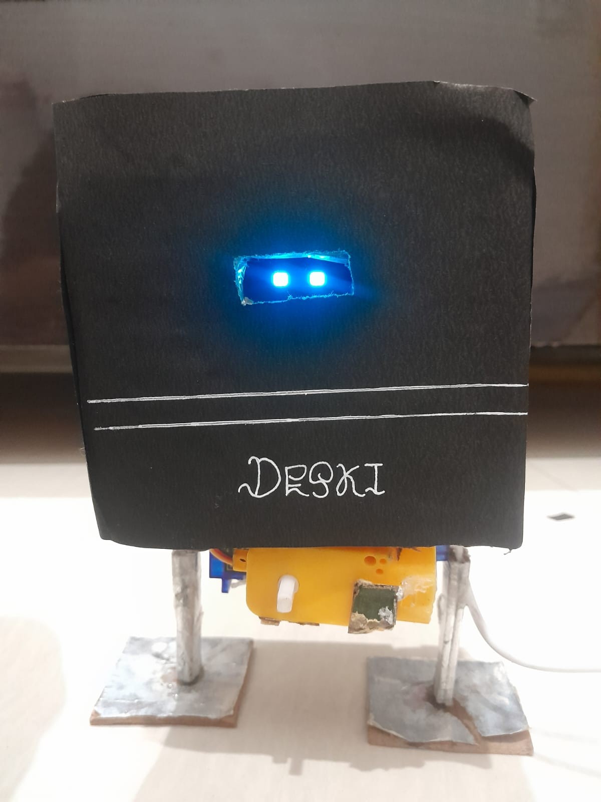 Fotografía de CraftyMind1020 de Deski V1 completo, con carcasa negra artesanal, ojos OLED azules, dos patas y pies planos.