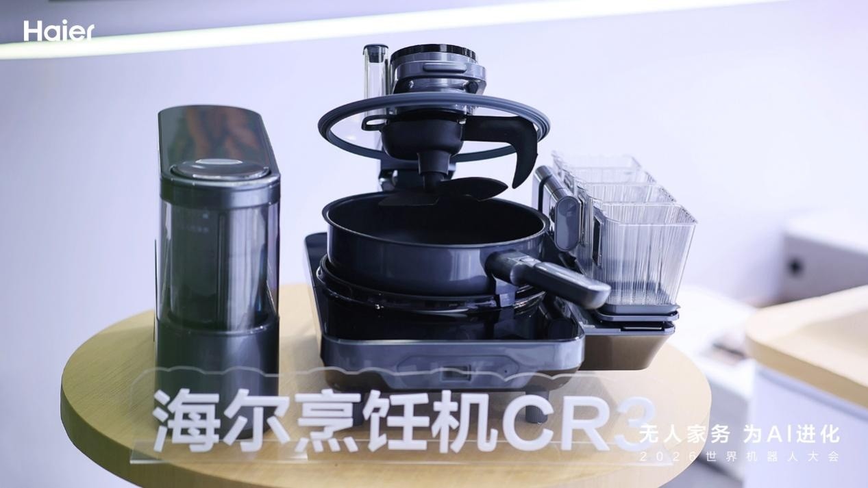 Imagen oficial de Haier del robot de cocina CR3 completo sobre una mesa amarilla, con los módulos de ingredientes y cocción.