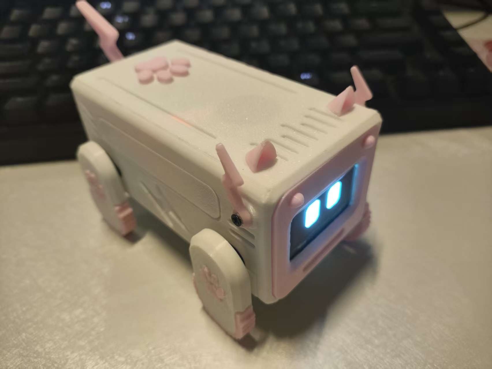 Fotografía del constructor de Xiaozhi ESP32 Pet completo, con carcasa rosa, pantalla facial y cuatro patas, sobre un escritorio.
