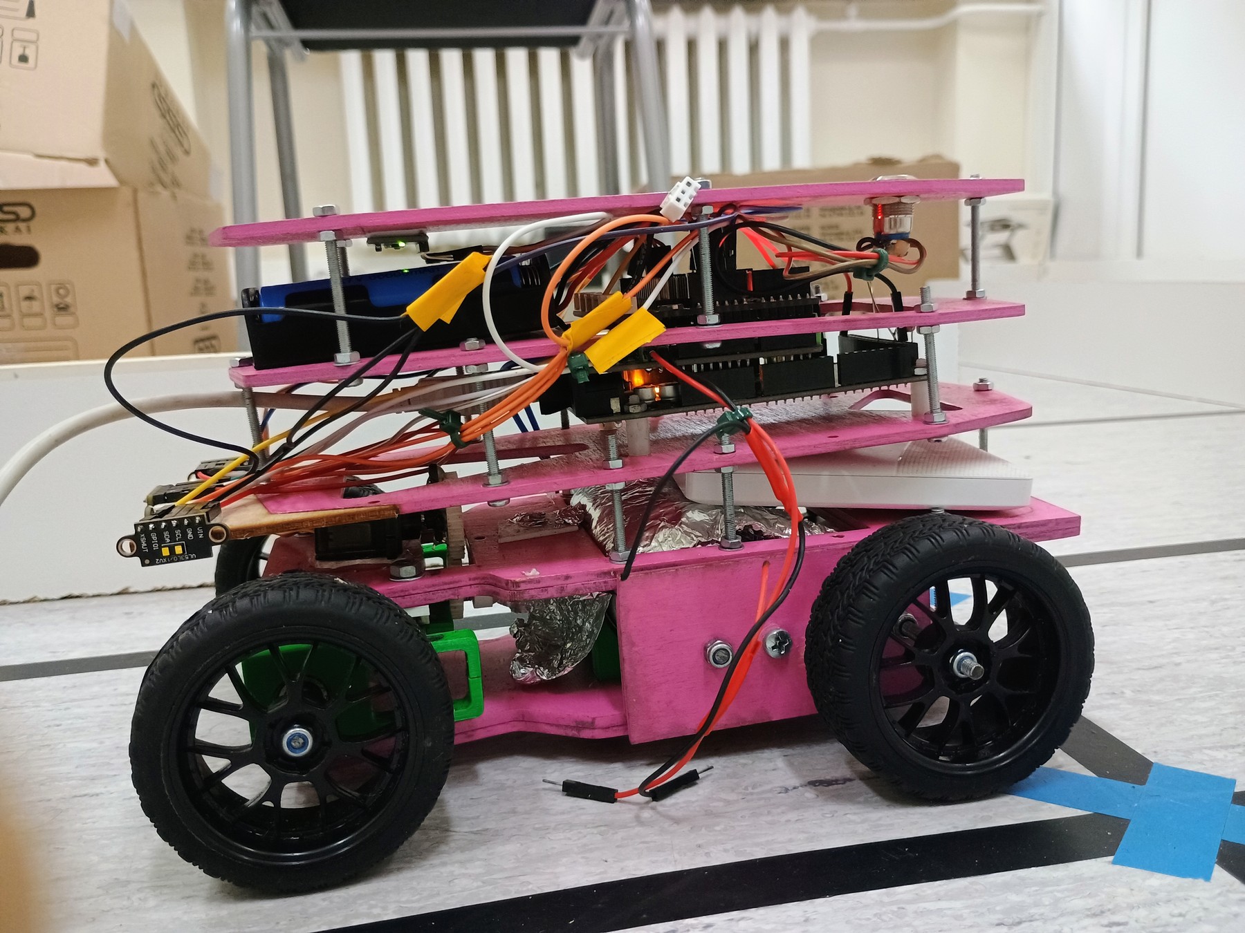 Fotografía de KU STEAM Pinkies de su coche robot completo visto de lado, con chasis rosa por niveles, cuatro ruedas y cableado visible.