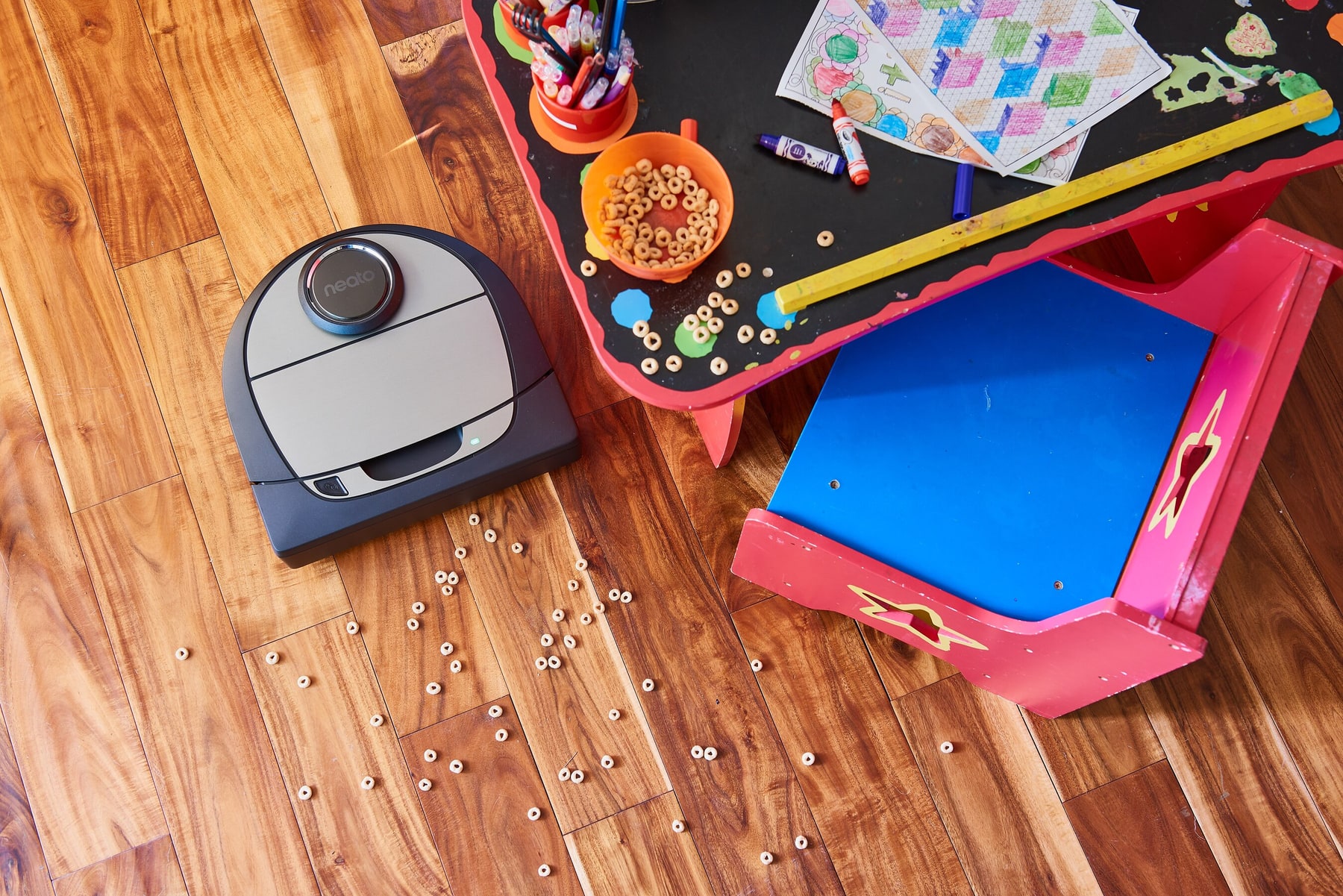 Imagen oficial del Neato Botvac D7 Connected en un suelo de madera junto a una mesa infantil.