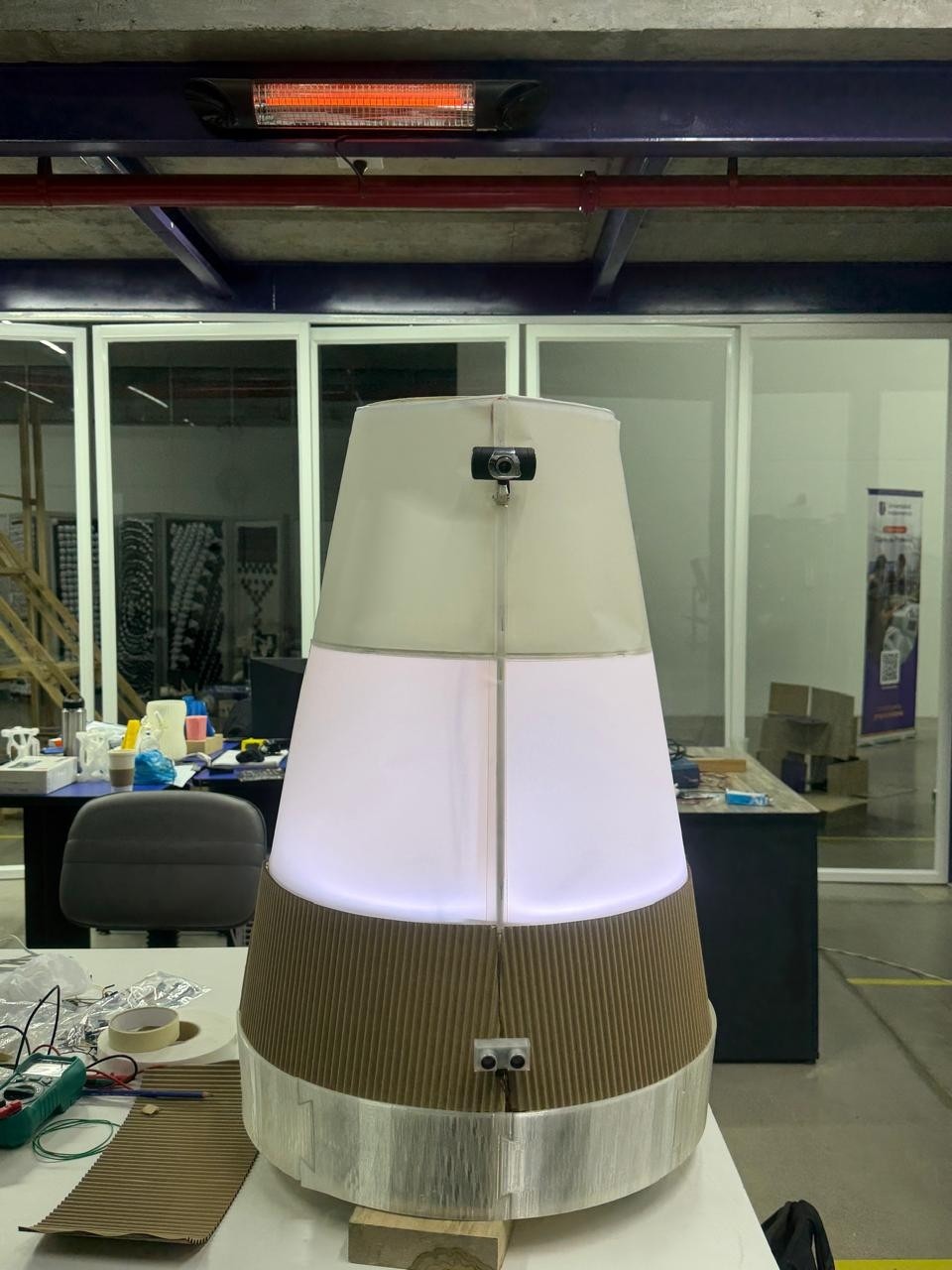 Fotografía de Nicolas Lara del robot completo, con cuerpo de madera y cubierta translúcida iluminada sobre su base móvil.