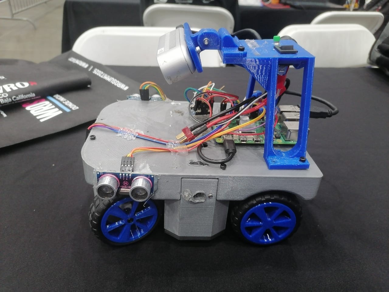 Fotografía del Equipo Octobots de Octoneer completo, con cuerpo gris, cuatro ruedas azules y un soporte elevado de componentes.