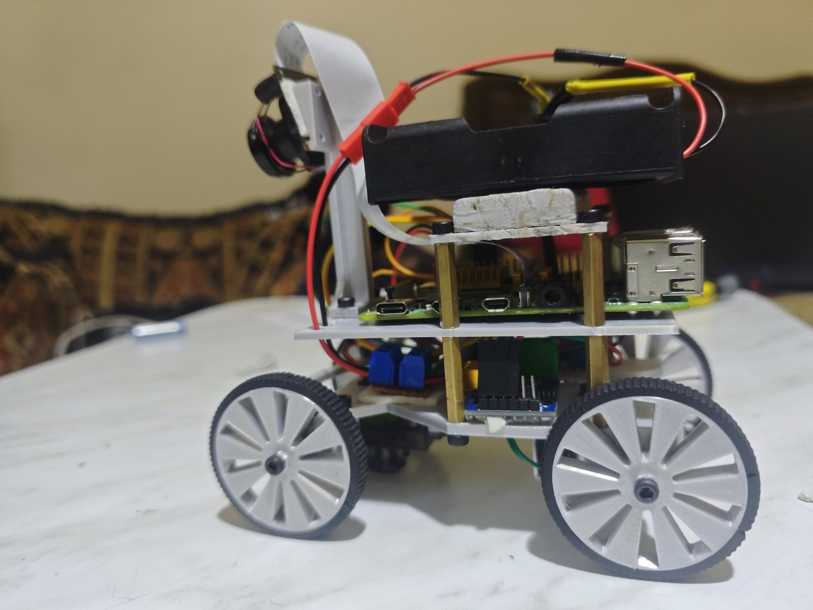 Fotografía de The Red Castle de su coche robot completo visto de lado, con cuatro ruedas grises, cámara elevada y chasis de varios niveles.