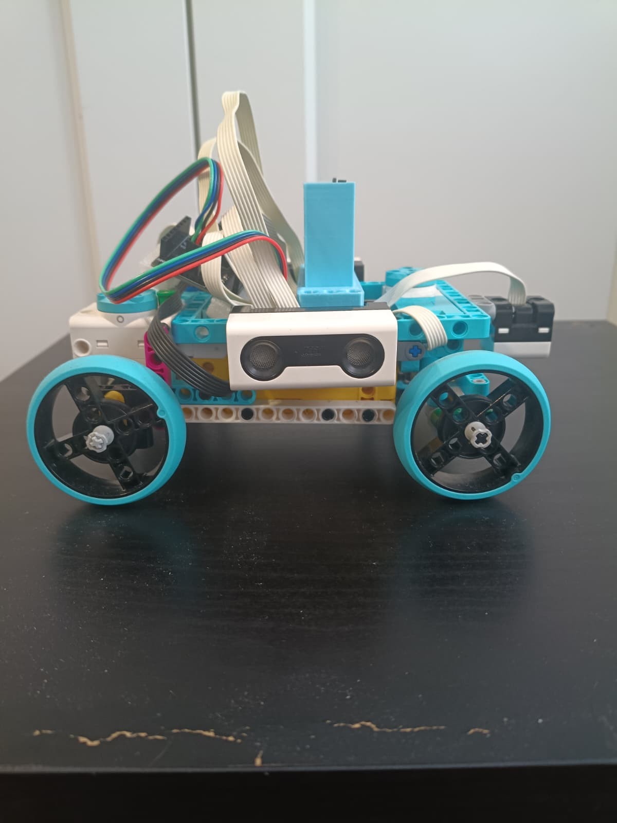 Fotografía de RoboTronics Bilbao de su coche robot completo visto de lado, con piezas claras y azules, cuatro ruedas y sensores visibles.
