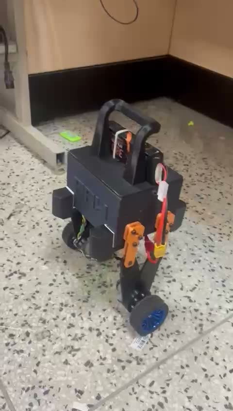 Fotograma del vídeo de Sndcooper con PAW completo, cuerpo negro, patas articuladas naranjas y dos ruedas, en un ensayo sobre el suelo.