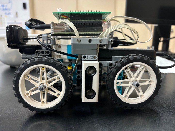 Fotografía de Teikyo RoboLet’sGo de su coche robot completo visto de lado, con piezas LEGO, cuatro ruedas y electrónica sobre el chasis.
