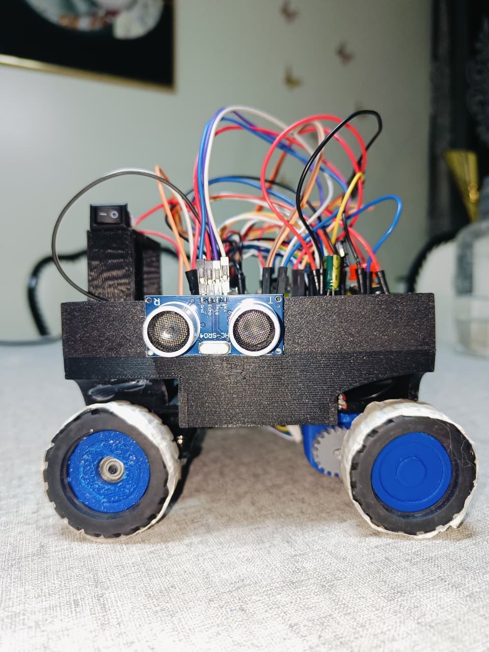 Fotografía de Vitality de su coche robot completo, con cuatro ruedas azules, electrónica visible y sensor ultrasónico lateral.